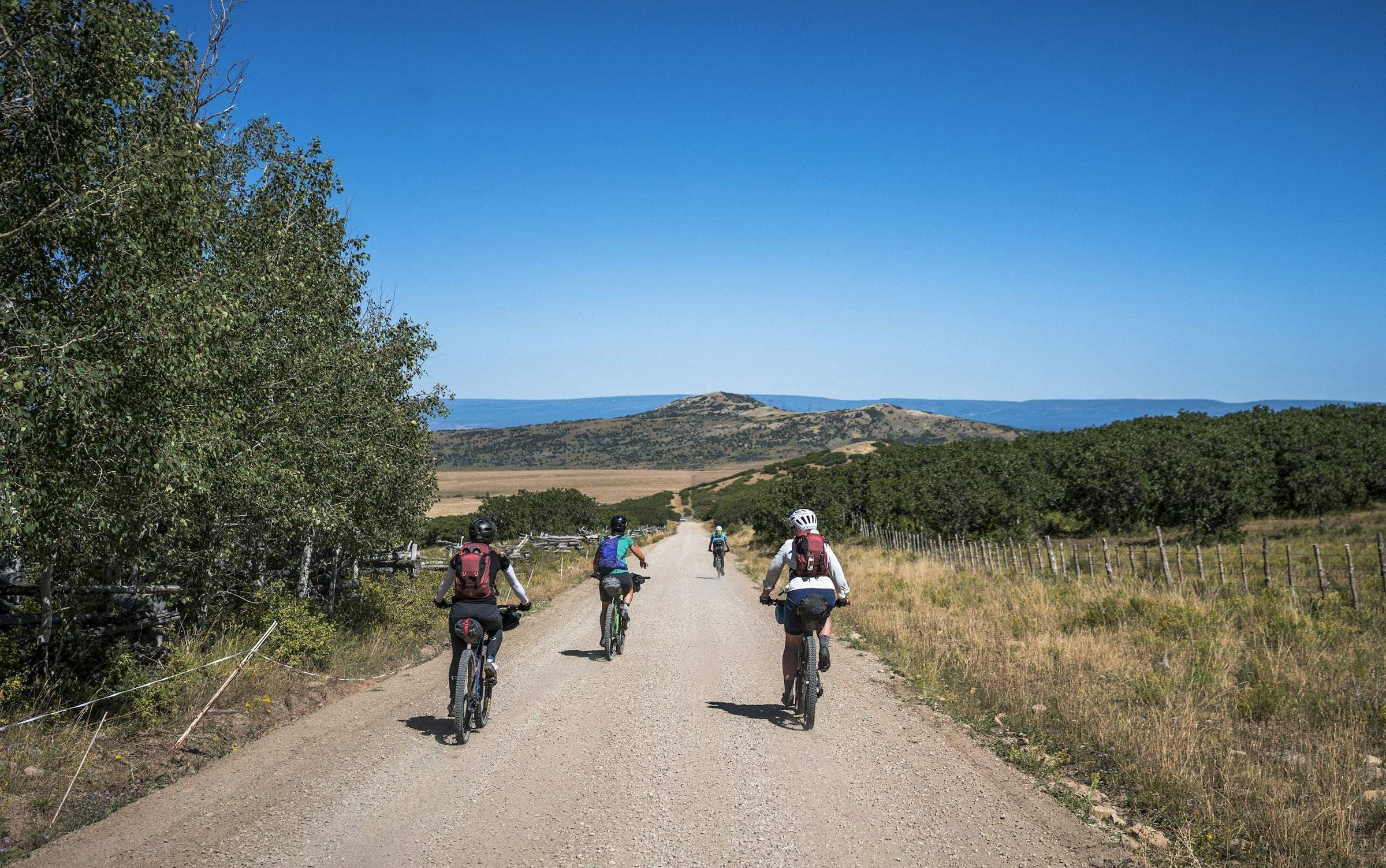 Vier bepakte fietsers, van achteren, op een onverharde weg richting de heuvels.